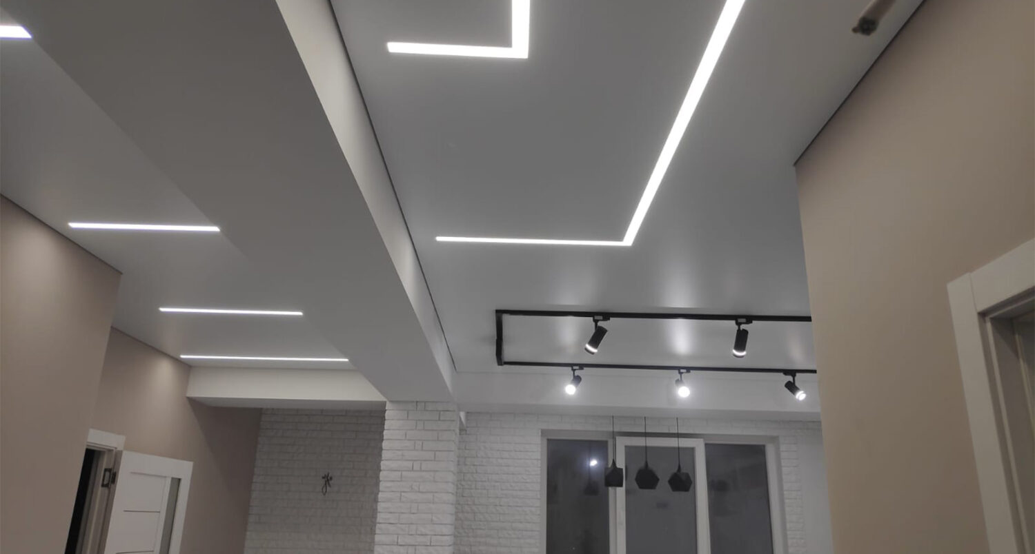 Tavan extensibil cu linii LED albe încastrate și șină cu spoturi negre, într-un living cu perete din cărămidă albă