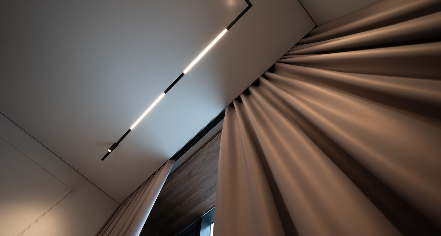 Șină magnetică neagră cu modul LED liniar pe tavan extensibil alb, deasupra unei draperii bej în valuri